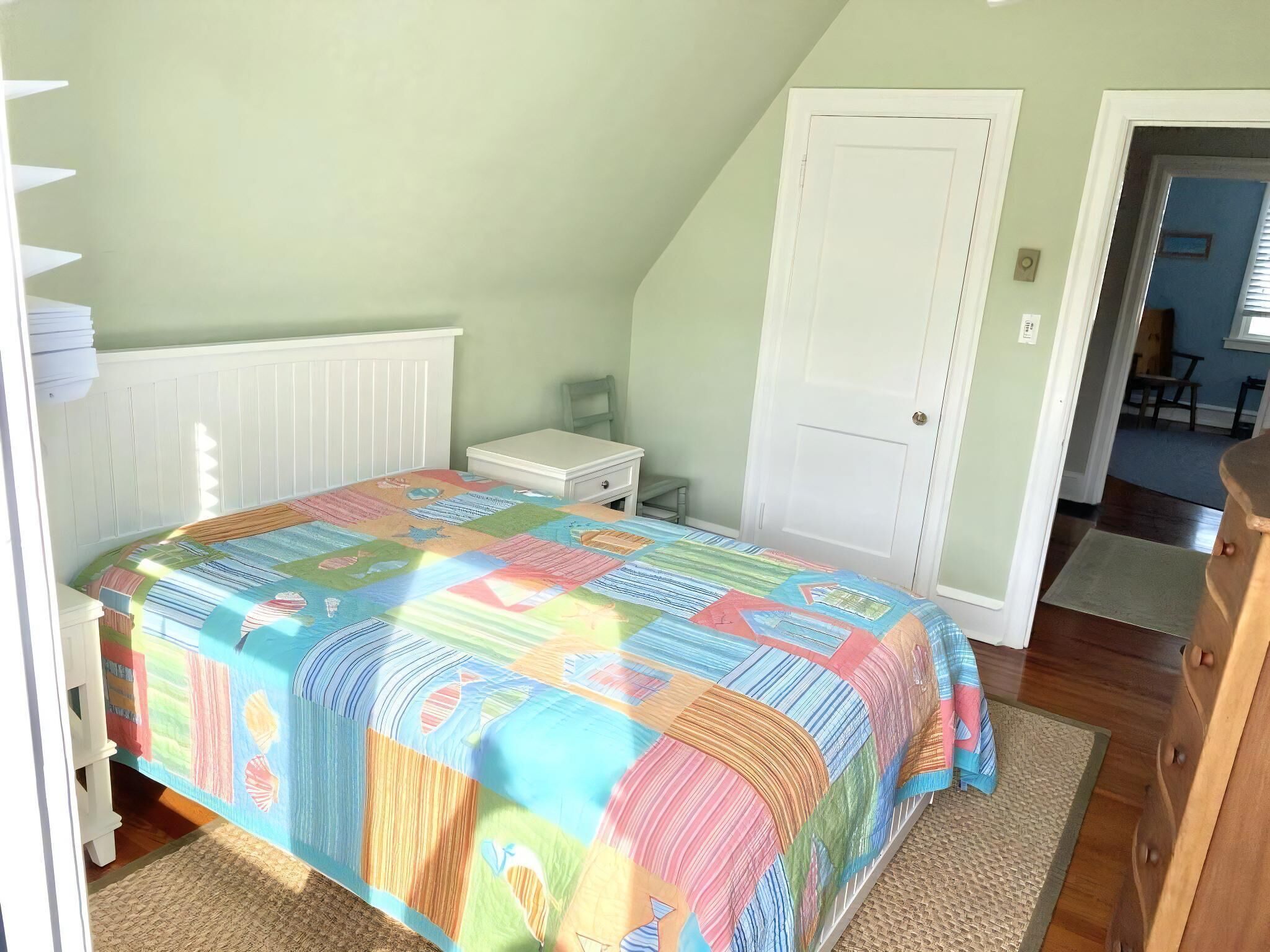 A bedroom with a bed, a nightstand, a door, and a view of another room.