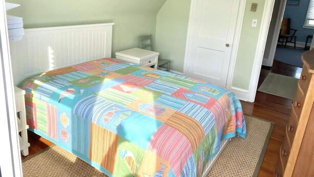 A bedroom with a bed, a nightstand, a door, and a view of another room. - LBI vacation rental property (Brant Beach)