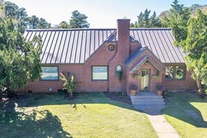 A brick house with a metal roof, a front porch, and a small garden. - Bostwick's Magnolia Manor (Wanchese)