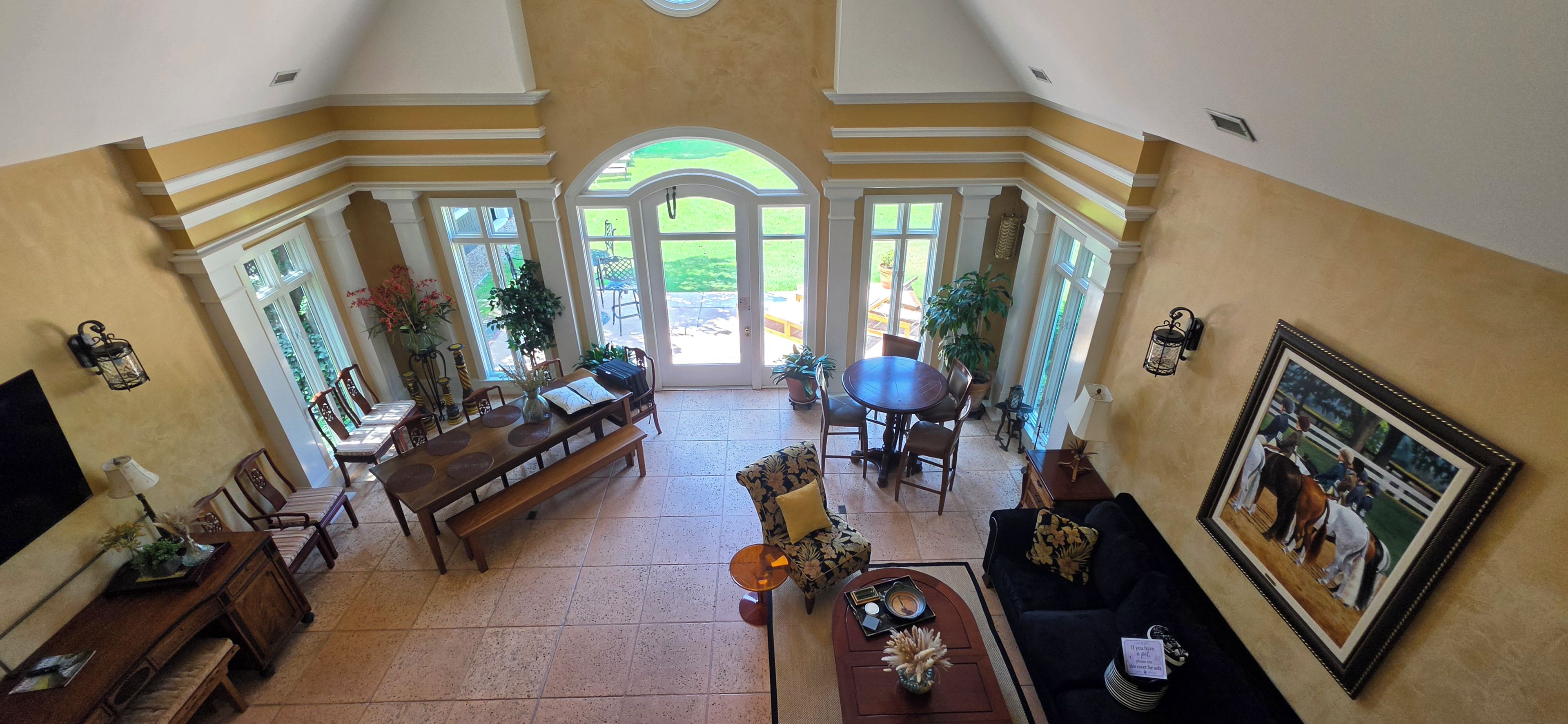 A spacious living area with a dining table, chairs, a sofa, and a coffee table. There are large windows and doors leading to an outdoor patio.