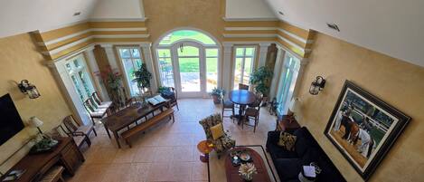 A spacious living area with a dining table, chairs, a sofa, and a coffee table. There are large windows and doors leading to an outdoor patio.