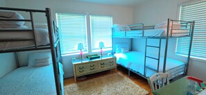 A dormitory room with bunk beds, a dresser, and a window with blinds.