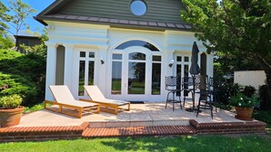 Uma casa com varanda, duas poltronas, uma mesa e um espaço de estar com cadeiras e guarda-sol.