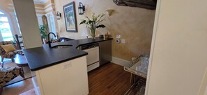 A compact kitchen with a dishwasher, a sink, and a small countertop. There is a vase with flowers on the counter, and a framed picture on the wall.