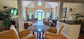 A spacious living room with a glass-top coffee table, comfortable seating, and a view through a large arched doorway to an outdoor area.