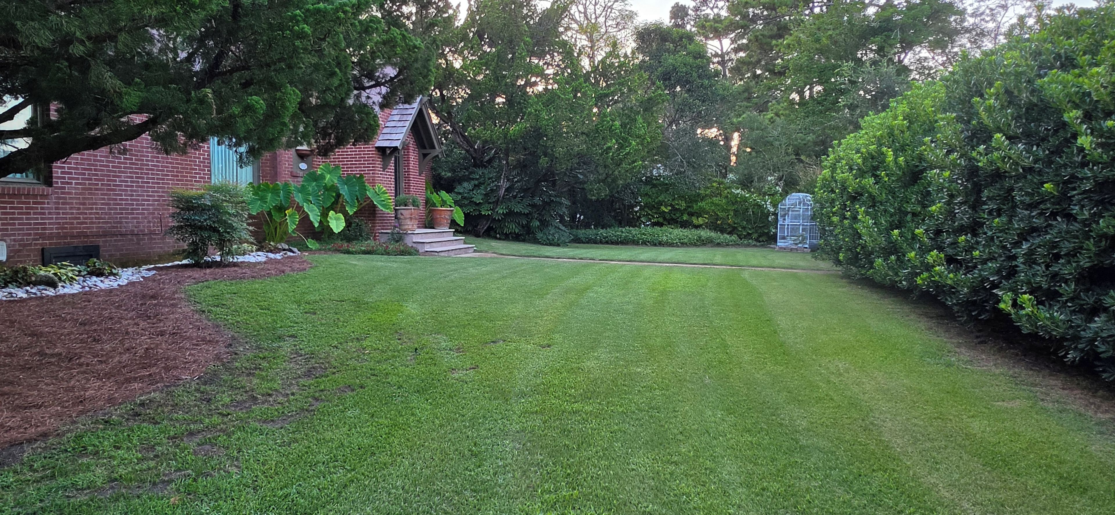 A well-maintained lawn with a brick house and a birdhouse.