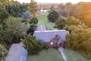 A large house with a sloped roof and a brick chimney, surrounded by a well-maintained lawn and dense trees.