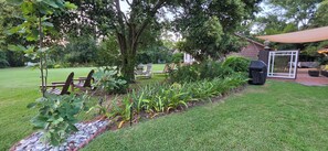 A well-maintained garden with a lawn, a wooden deck with chairs, and a barbecue area.