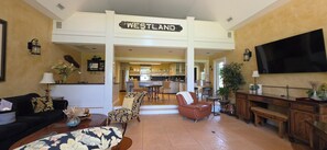 A spacious living room with a Westland sign, a dining area, kitchen, and a TV mounted on the wall.