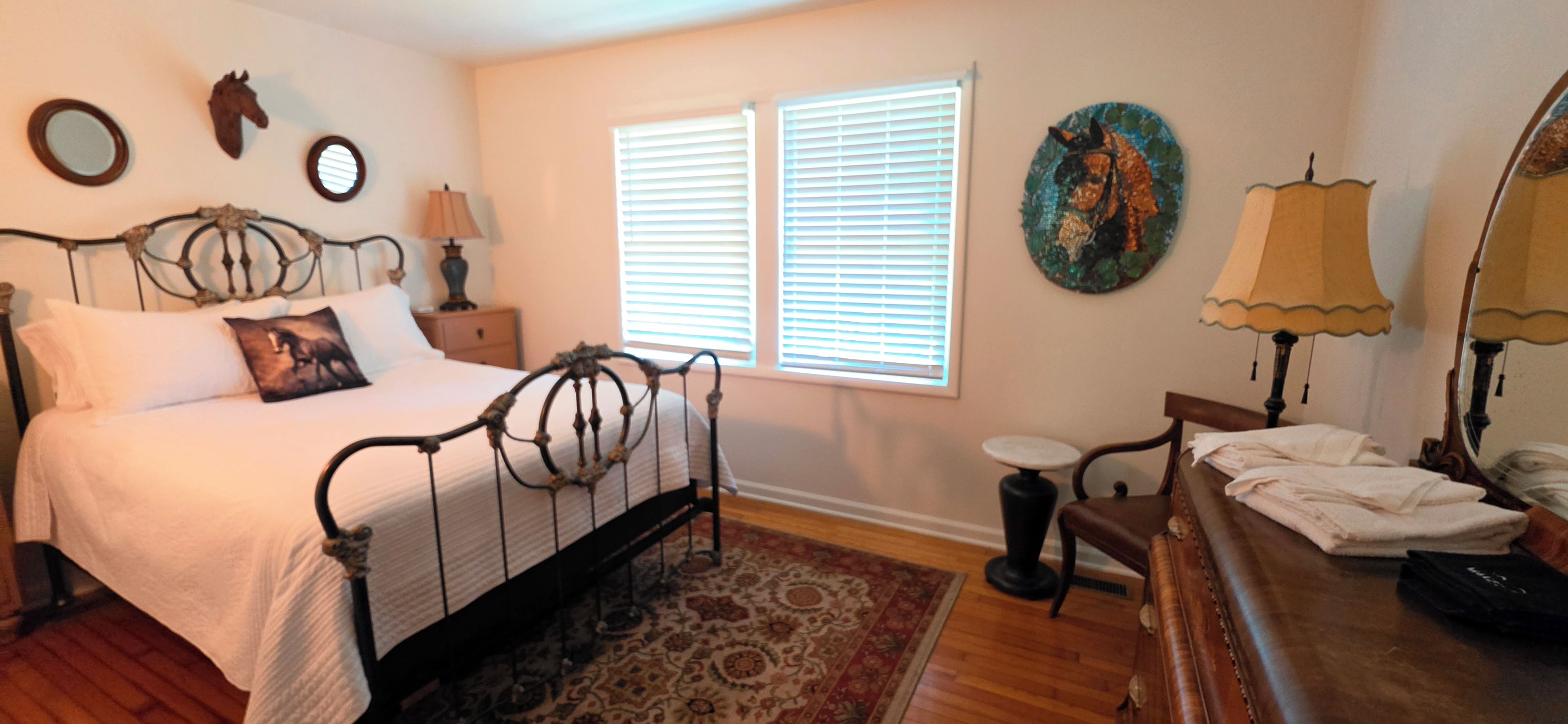Une chambre à coucher comprenant un lit, des tables de chevet, une commode, une chaise, une coiffeuse, un miroir et une fenêtre avec des stores.
