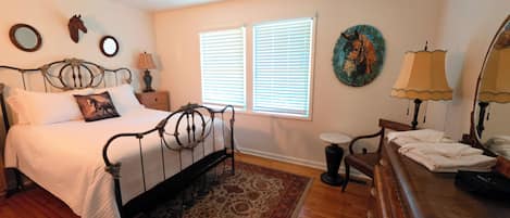 A bedroom with a bed, bedside tables, a nightstand, a chair, a dresser, a mirror, and a window with blinds.