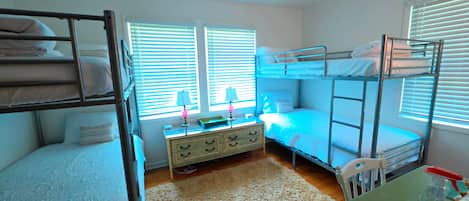 Une chambre de dortoir avec des lits superposés, une commode, une lampe et une fenêtre avec des stores.