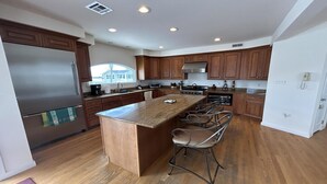 A modern kitchen with a central island, stainless steel appliances, and wooden cabinetry. - Large Contemporary Ocean Block Home (Loveladies)