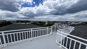 A rooftop with white railings, a clear sky, and residential buildings in the background. - Large Contemporary Ocean Block Home (Loveladies)