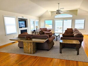 A spacious living room with a fireplace, large windows, and a ceiling fan. - Large Contemporary Ocean Block Home (Loveladies)