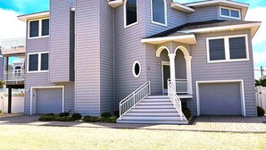 A two-story house with a garage, a covered porch, and a staircase leading to the entrance. - Large Contemporary Ocean Block Home (Loveladies)
