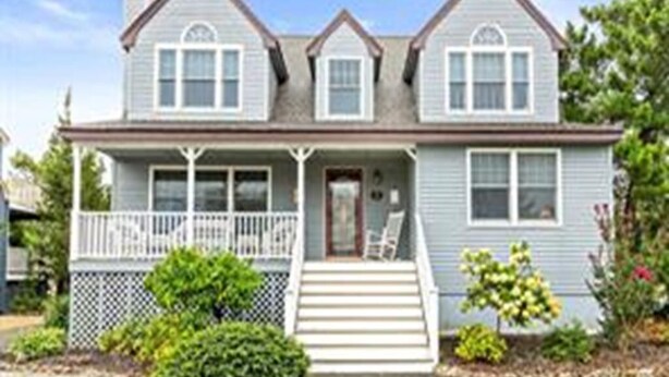 A two-story house with a front porch, a chimney, and a small garden with bushes and flowers. - 5 bedroom accommodation in Long Beach Township (Long Beach Township)