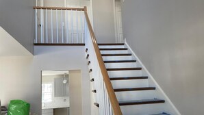 A staircase with wooden handrails and white walls, leading to a room with a kitchen area visible through an open door. - 5 bedroom accommodation in Long Beach Township (Long Beach Township)