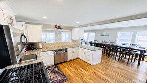 A modern kitchen with granite countertops, white cabinetry, a stainless steel range, and a dining area with wooden chairs and a table.
