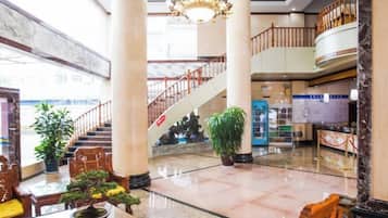 A spacious lobby with a marble floor, a staircase, and a reception desk.