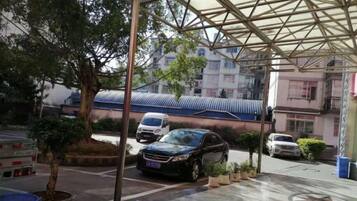 Un área de estacionamiento techada con coches, un árbol y un edificio con techo azul al fondo.