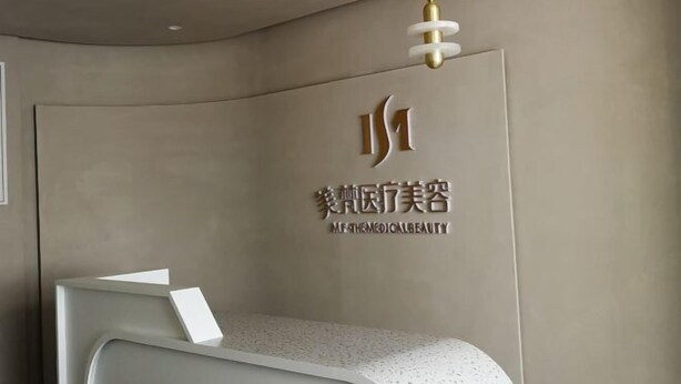 A reception desk with a modern design, a logo on the wall, and a ceiling light fixture. - Pu'er Kunman Hotel (Pu'er)