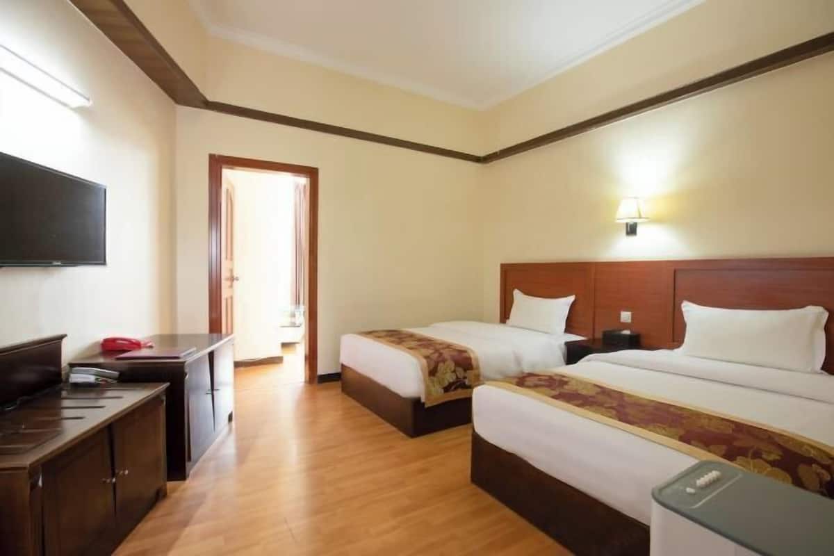 Une chambre d’hôtel avec deux lits, un bureau, un téléviseur à écran plat et une lampe.