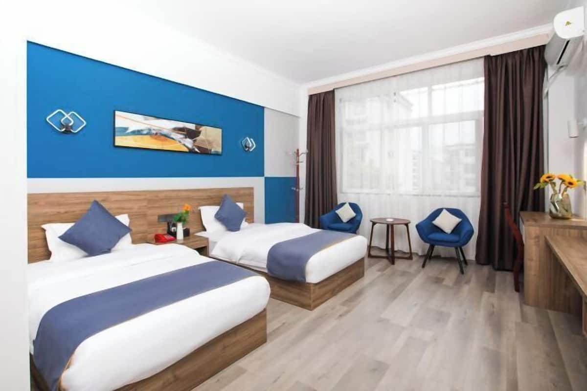 Une chambre d’hôtel avec deux lits, un bureau, une chaise et une fenêtre avec des rideaux.