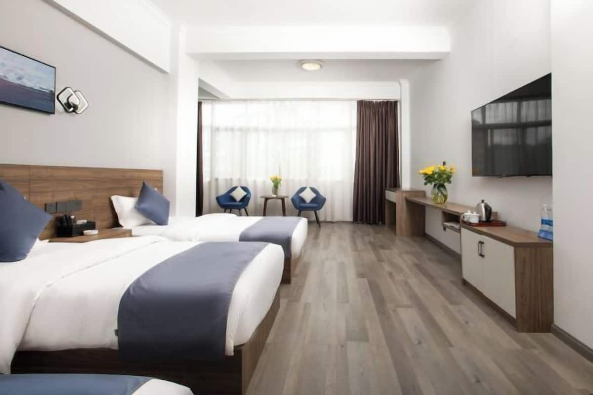 Une chambre d’hôtel avec deux lits, une télévision, un bureau et une fenêtre avec des rideaux.