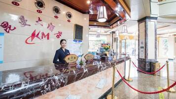 A hotel reception desk with a marble counter, a receptionist, and a red rope barrier.