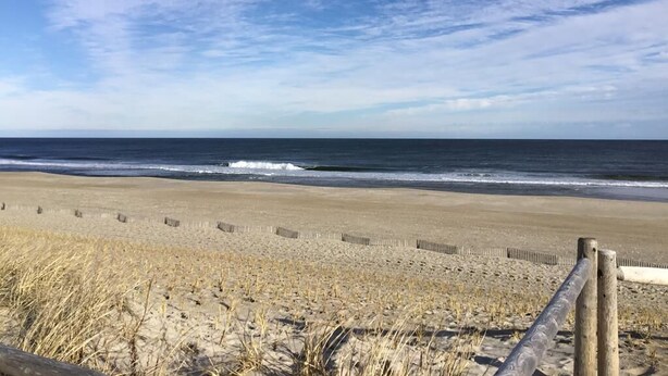 Une plage avec une clôture en bois et des vagues de l’océan.