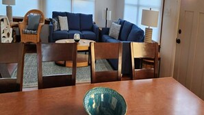 Un salon avec un canapé bleu, des chaises en bois, une table basse ronde et un saladier en verre.