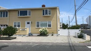 A two-story residential building with a front porch, a small garden with white flowers, and a white fence.