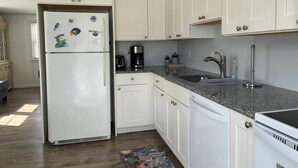 A kitchen with white cabinets, a refrigerator, a coffee maker, and a sink.