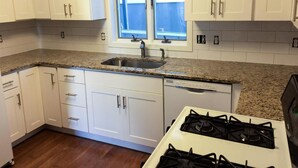 A kitchen with white cabinets, a granite countertop, a stainless steel sink, a window with blinds, and a gas stove.