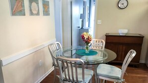 A dining area with a glass table, white chairs, a vase of flowers, and a clock on the wall.