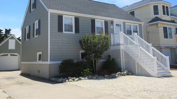 A two-story house with a grey exterior, white trim, and a small front yard with a tree and a white staircase.