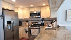 A modern kitchen with white cabinets, stainless steel appliances, a granite countertop, and a tiled backsplash.