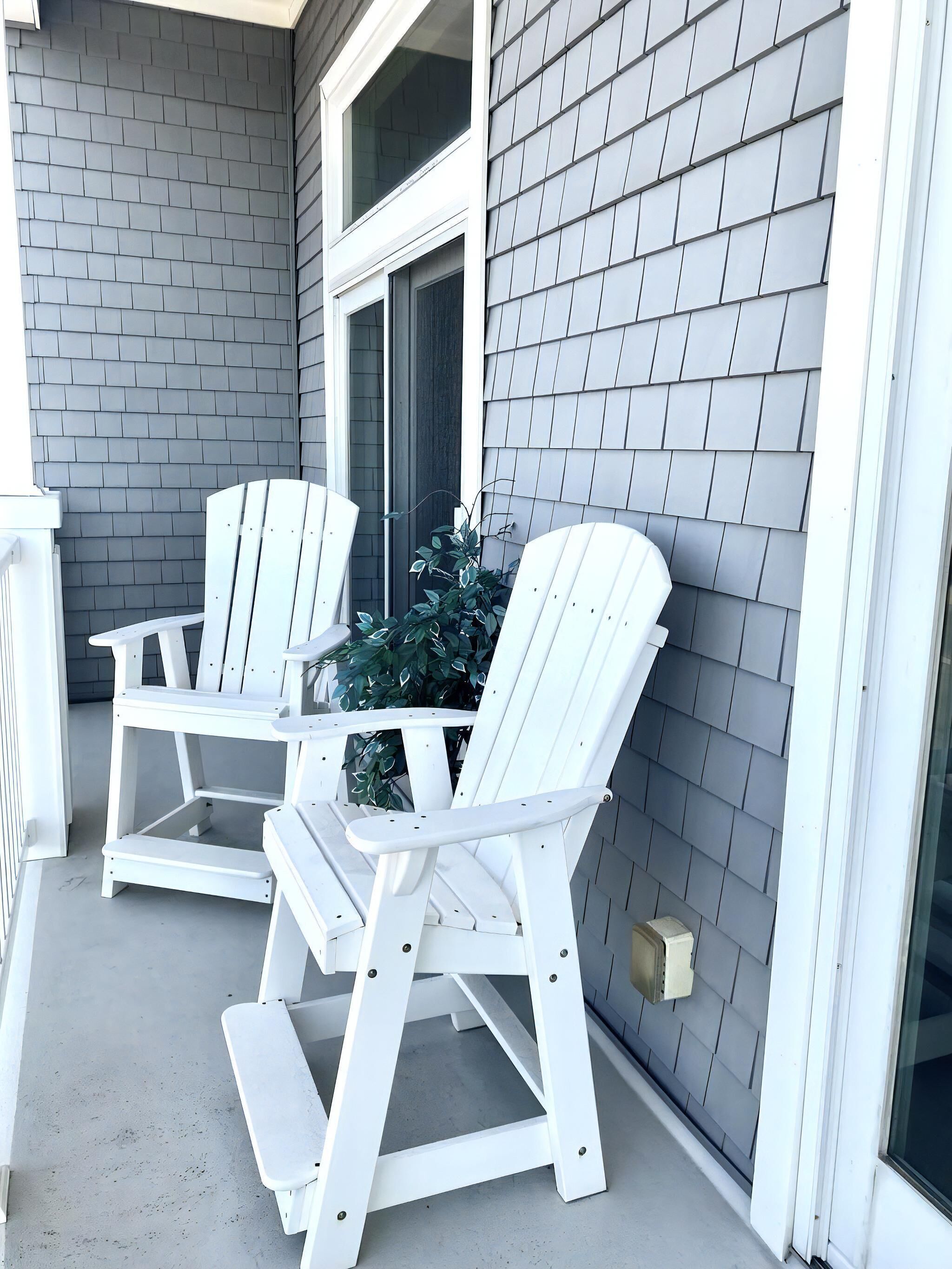 Une véranda avec deux fauteuils Adirondack et une petite table, une fenêtre et un mur en briques.