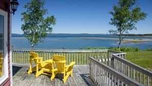 Une terrasse en bois avec des fauteuils Adirondack jaunes donnant sur un lac.