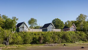 Une rangée de trois maisons, avec une clôture en bois en arrière-plan, le tout entouré de verdure.