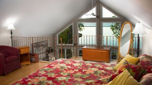 Une chambre avec un grand lit, une commode en bois, un fauteuil rouge, un miroir et un balcon donnant sur l’eau.