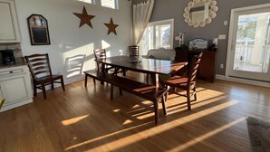 Un coin repas avec une table et des chaises en bois, un ventilateur de plafond et une grande fenêtre avec des rideaux.