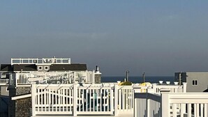 Une zone résidentielle côtière avec des clôtures et des bâtiments blancs, un ciel dégagé et la mer en arrière-plan.