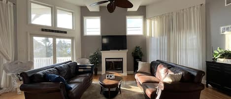 A spacious living room with two leather sofas, a coffee table, a fireplace, and a ceiling fan.