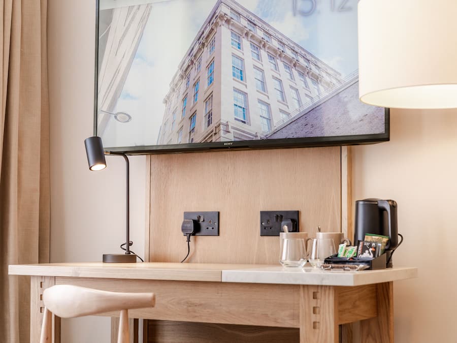 Habitación de hotel con un escritorio de madera, un televisor de pantalla plana en la pared, una lámpara y una cafetera.