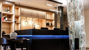 Een moderne receptiebalie met een houten toonbank, planken met flessen en glazen, en hangende hanglampen.