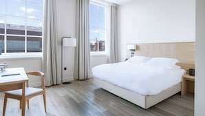 Hotelkamer met een groot bed, een bureau met stoel, een lamp en uitzicht op de stad door het raam.