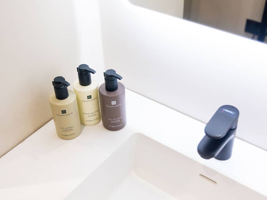 A bathroom sink with three bottles of skincare products and a modern faucet.