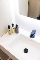 A bathroom sink with three bottles of skincare products and a modern faucet.
